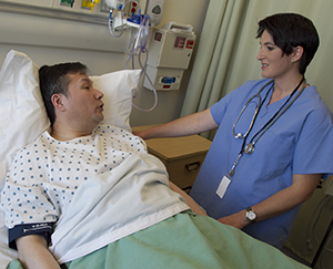 Hombre acostado en una cama de hospital, hablando con una proveedora de atención médica.