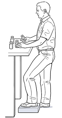 Hombre parado frente a una mesa de trabajo con un pie encima de un bloque.