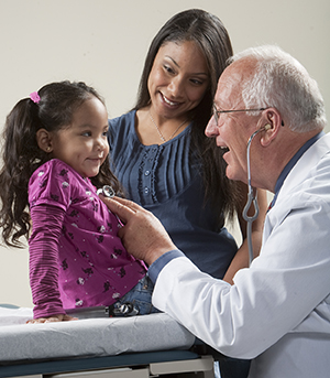 Proveedor de atención médica escuchando con un estetoscopio el pecho de una niña mientras una mujer los observa.